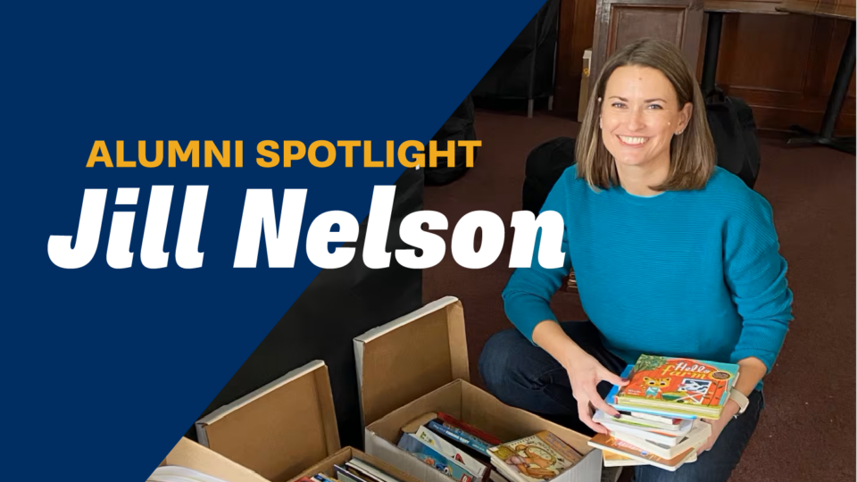 A woman smiling while holding a stack of childrens books, kneeling beside boxes of books. A banner reads, Alumni Spotlight Jill Nelson against a blue background.